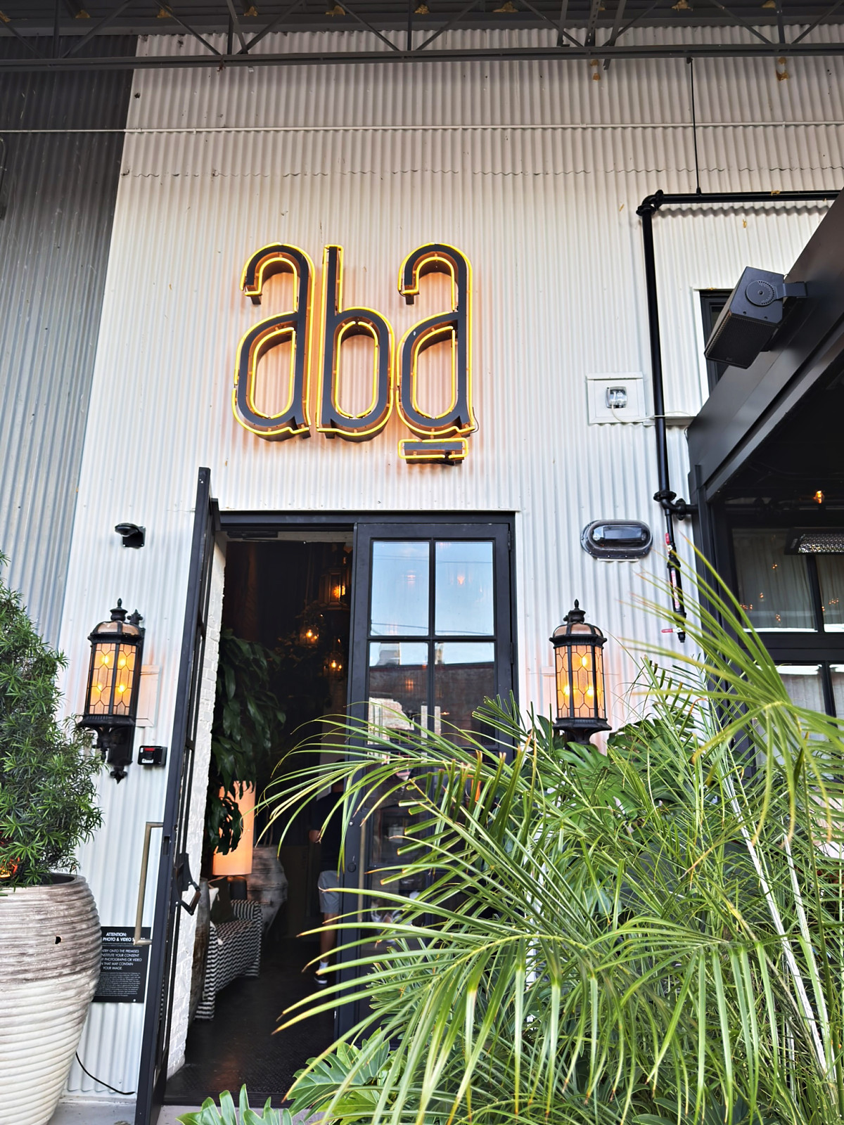 The illuminated gold aba sign above the restaurant's doorway with lanterns and palms in Wedgewood-Houston