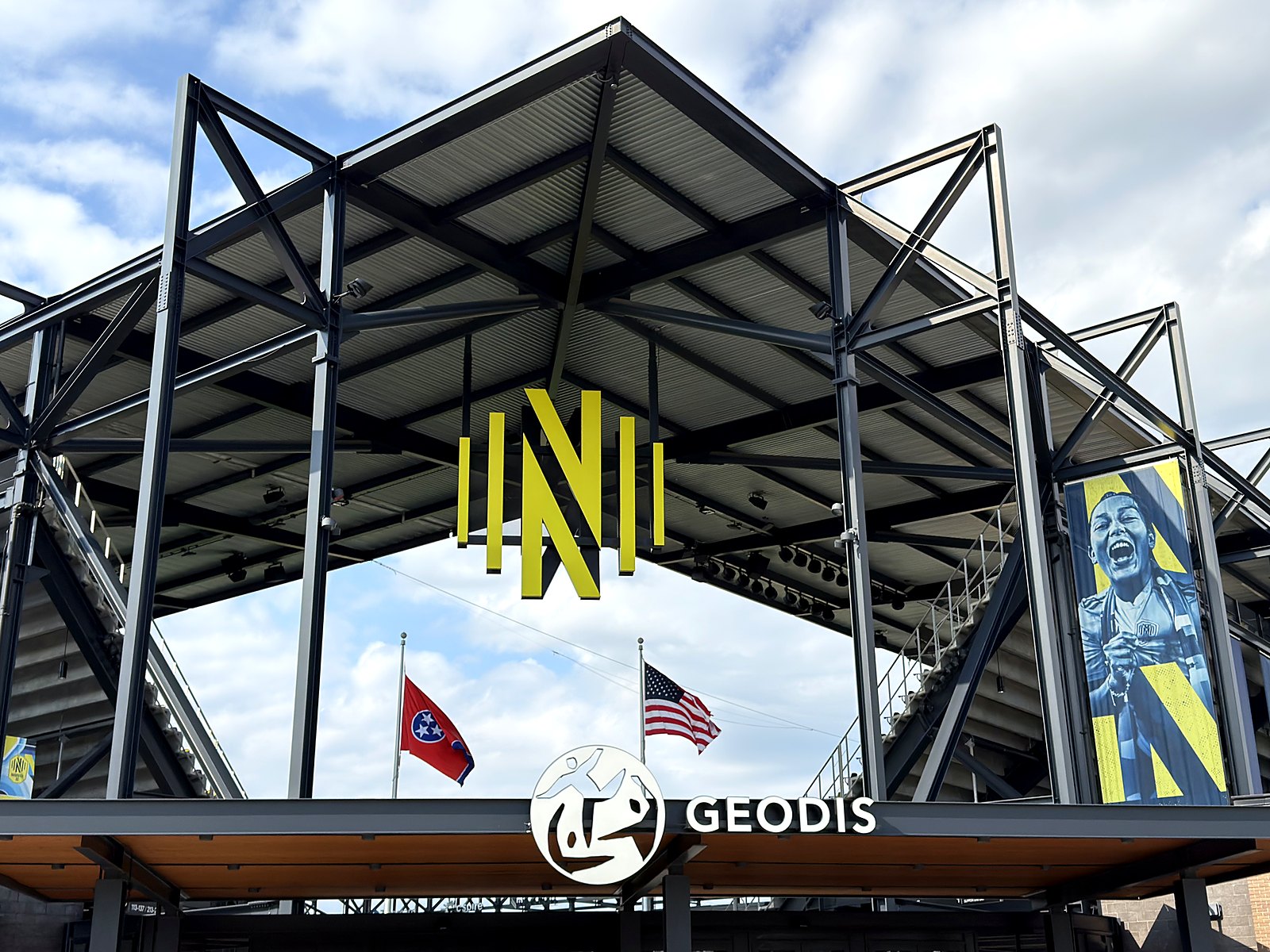 The Nashville SC gold crest above the GEODIS Park gate with Tennessee and American flags flying in Wedgewood-Houston
