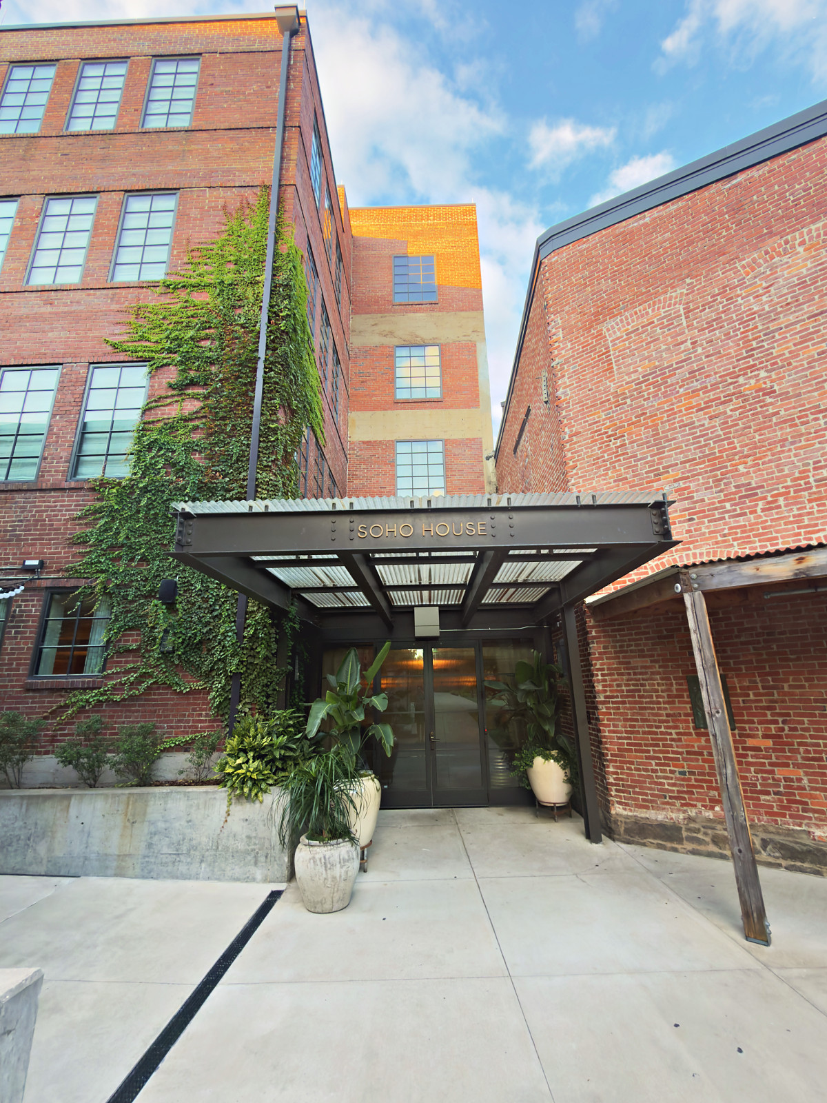 The canopied entrance to Soho House Nashville between ivy-covered brick warehouse buildings in Wedgewood-Houston