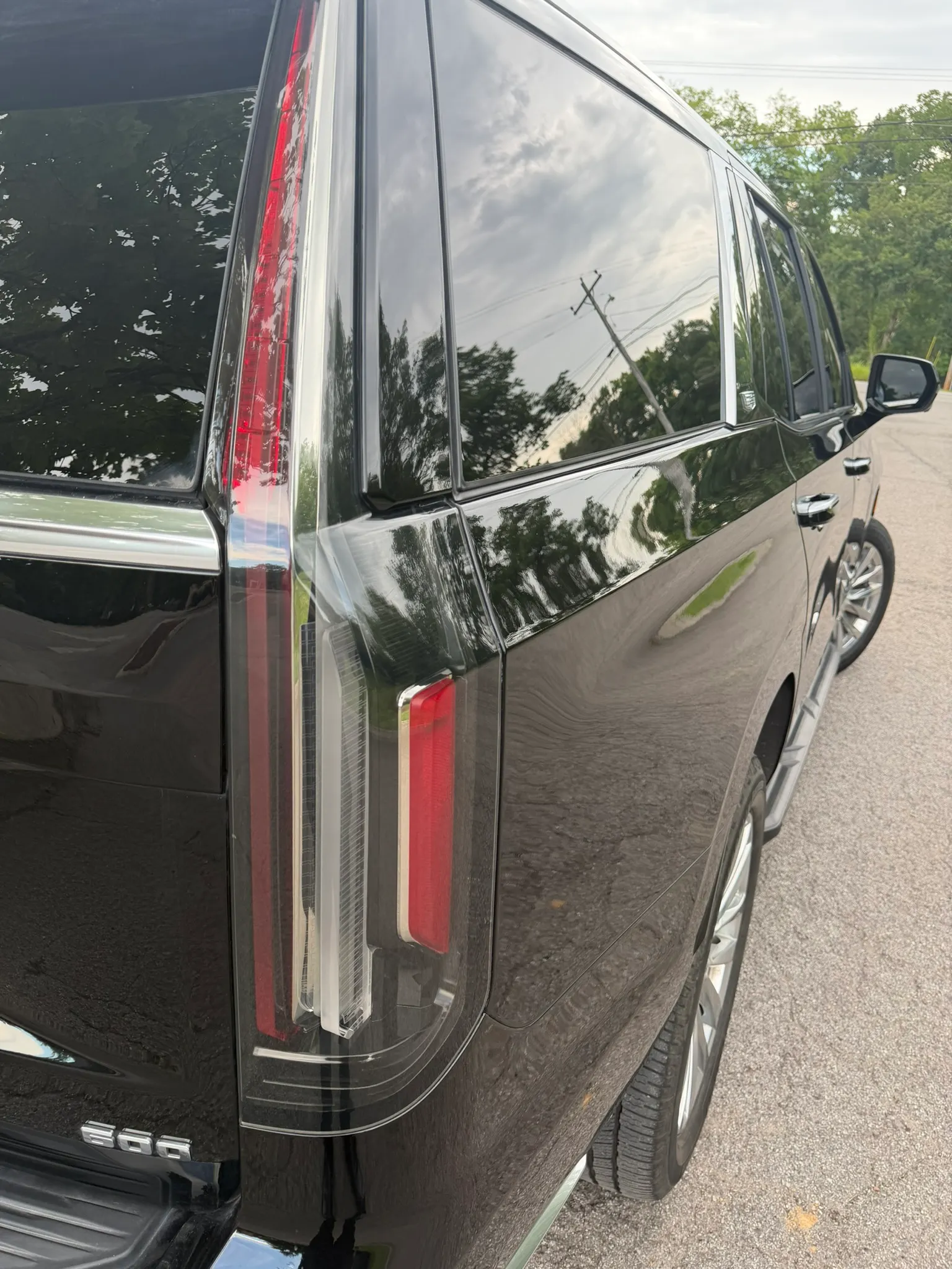 Close view of a black SUV rear quarter and taillight with trees reflected in the paint