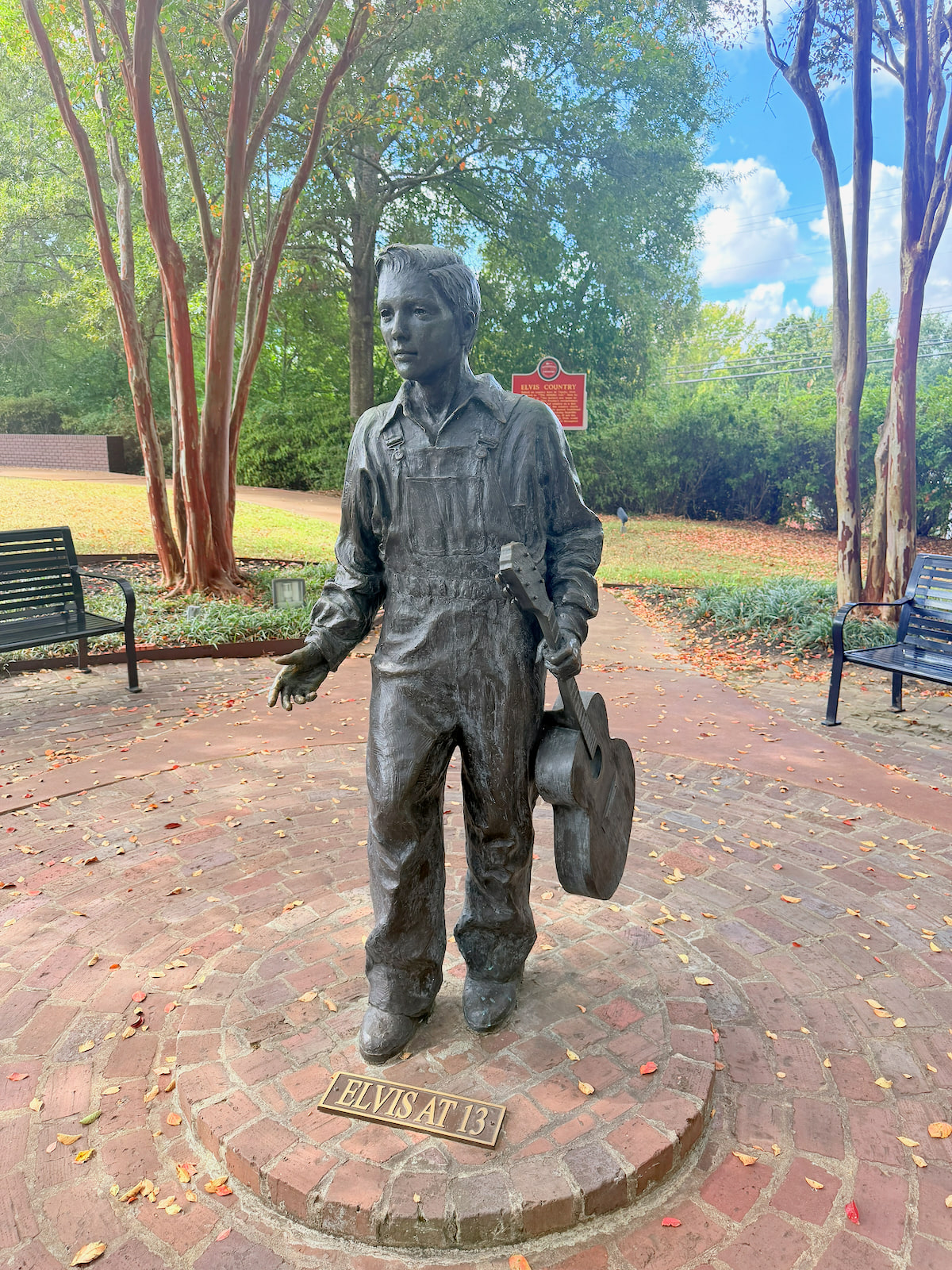 Elvis at 13 statue holding a guitar on a brick path at the Elvis Presley Birthplace in Tupelo